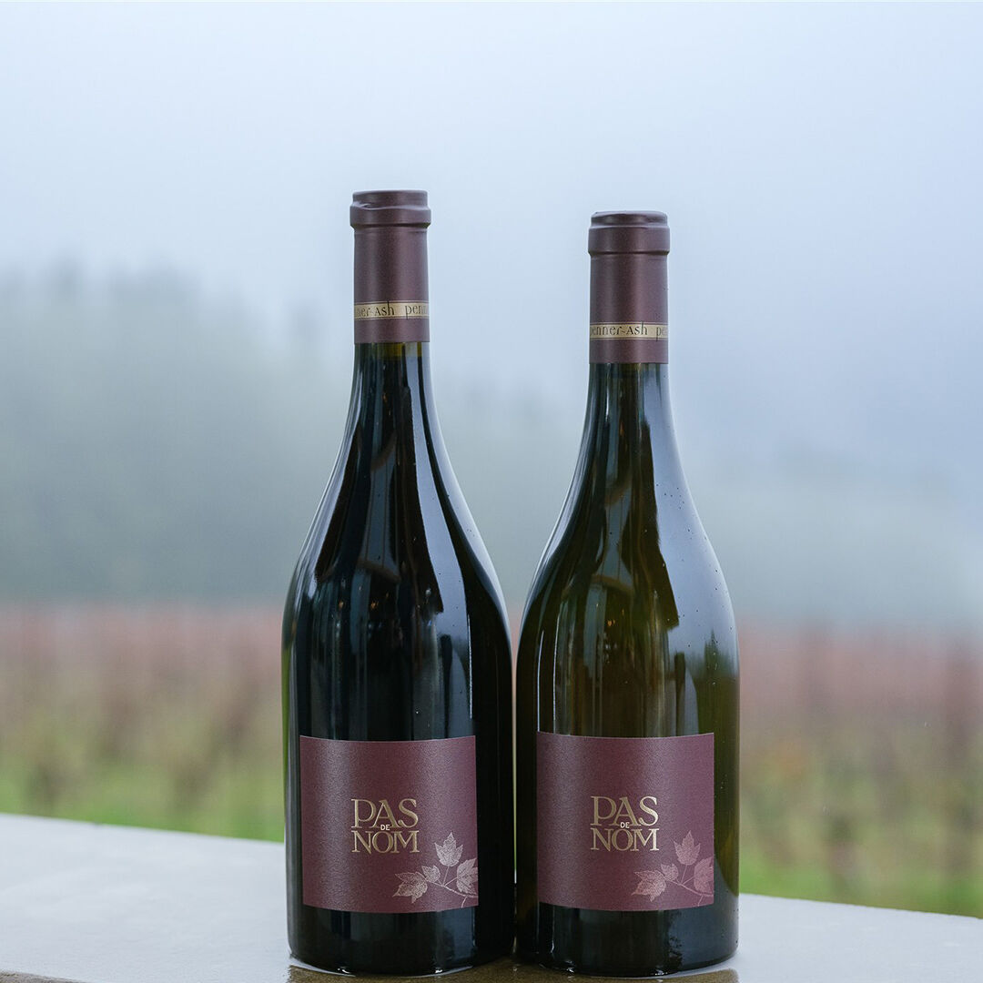 Pas De Nom Pinot Noir and Chardonnay bottles in front of Penner-Ash Estate Vineyard.